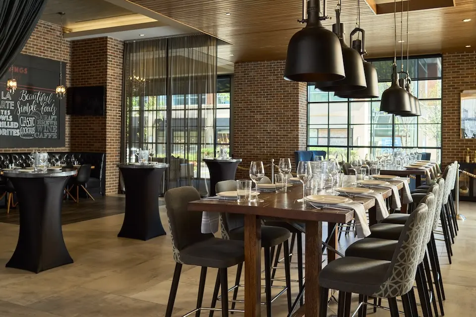 AKB - restaurant event space featuring a long wooden communal table with glassware and black cocktail tables