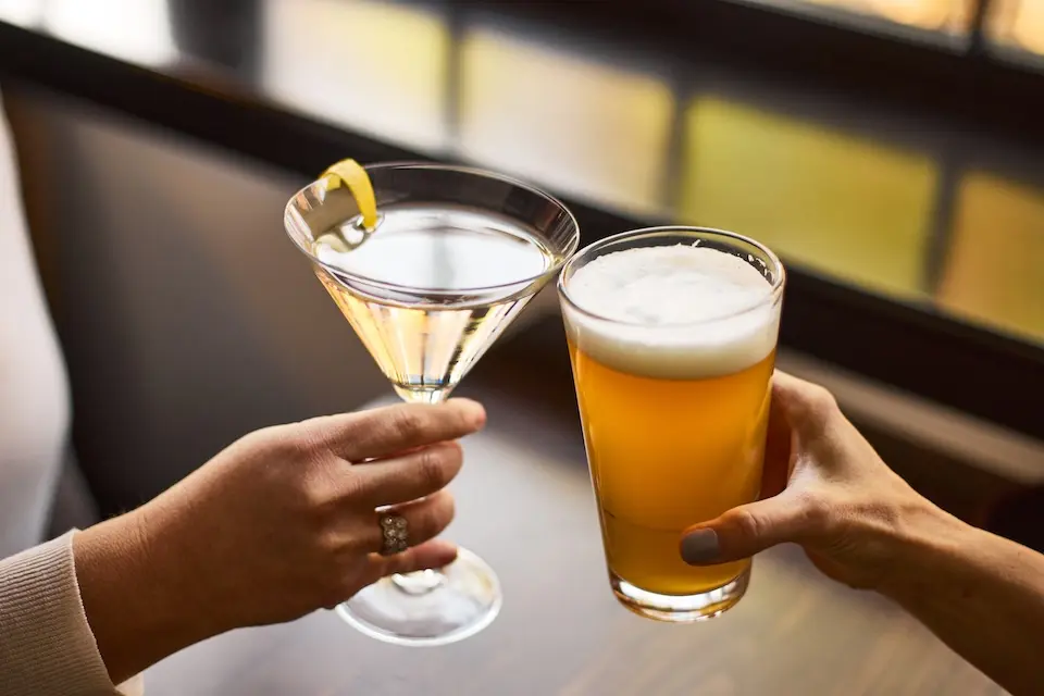 AKB Alexandria - two women toasting with a martini garnished with a lemon twist and a pint of beer with a frothy head