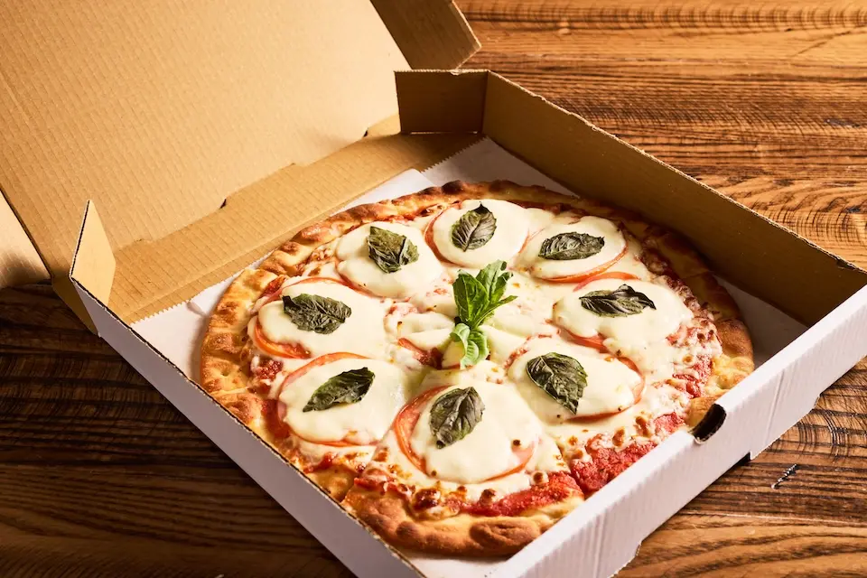AKB Florham Park - a fresh Margherita pizza topped with sliced mozzarella and fresh basil leaves inside an open cardboard takeout box