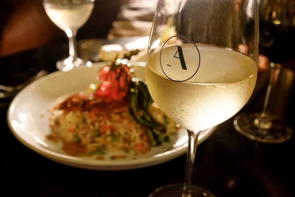 AKB Austin - a glass of white wine with the Archer logo next to a plate of salmon ceviche featuring rice, vegetables and a watermelon radish garnish