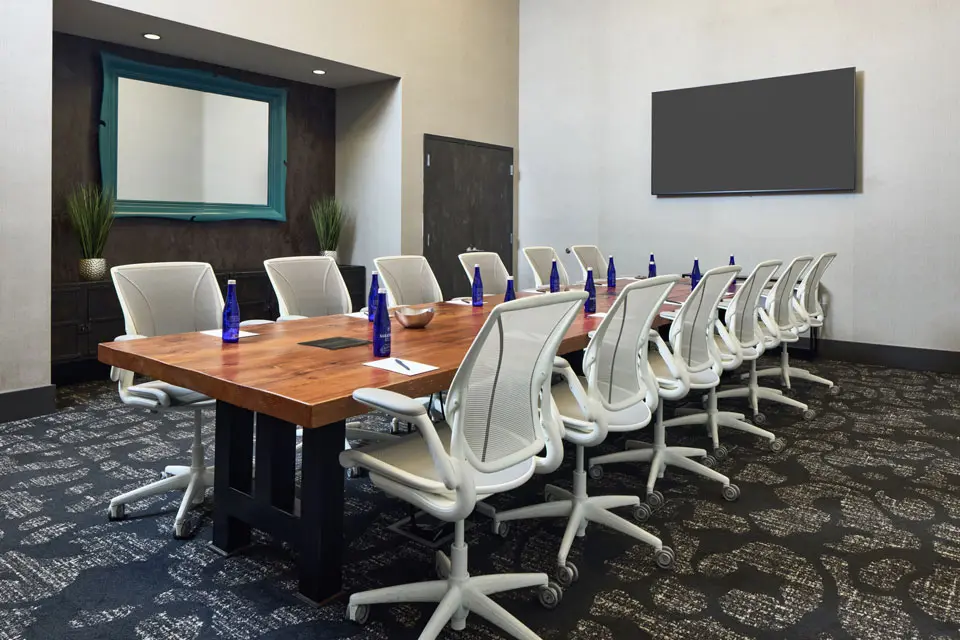 Boardroom - reclaimed wood table with ergonomic white mesh office chairs and a wall-mounted TV