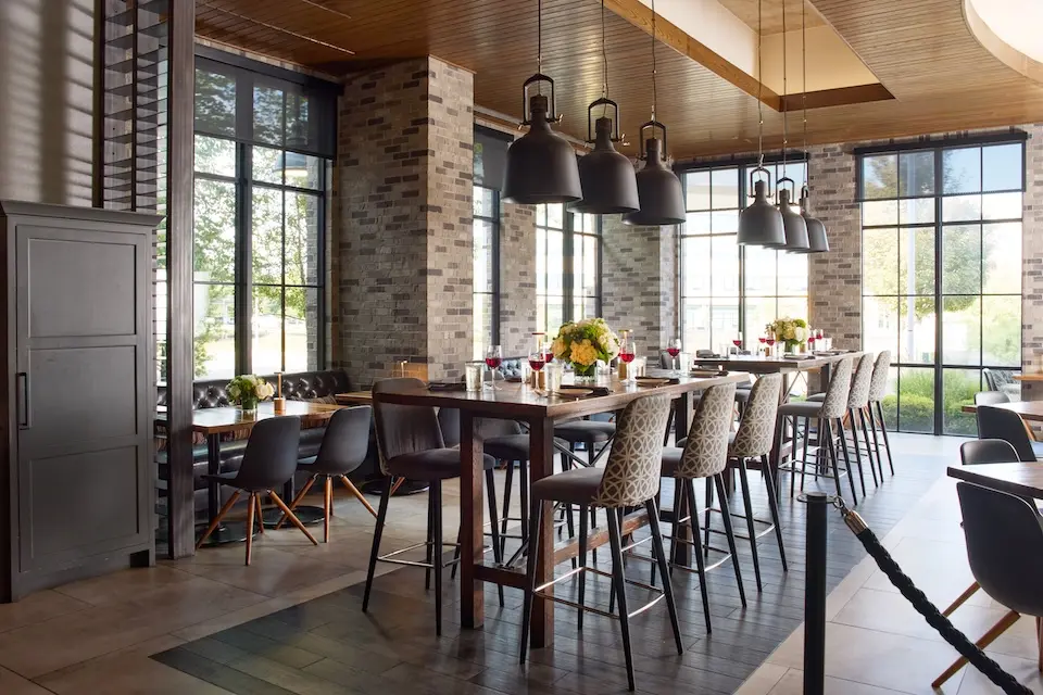AKB - semi-private dining venue with a long high-top table set with glassware and a white floral arrangement
