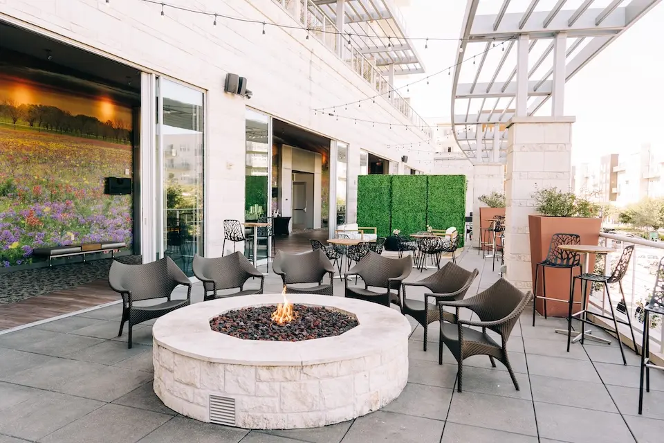 Terrace - lit stone fire pit surrounded by modern lounge chairs, high-top tables and string lights