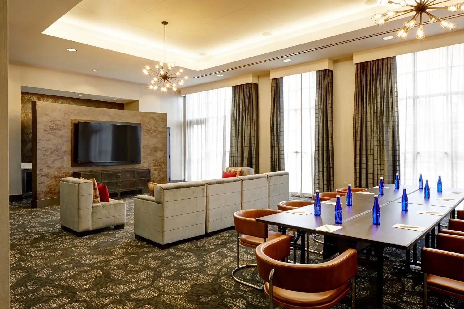 Hospitality Lounge - boardroom table with modular sectional, side lounge chairs and a wall-mounted TV