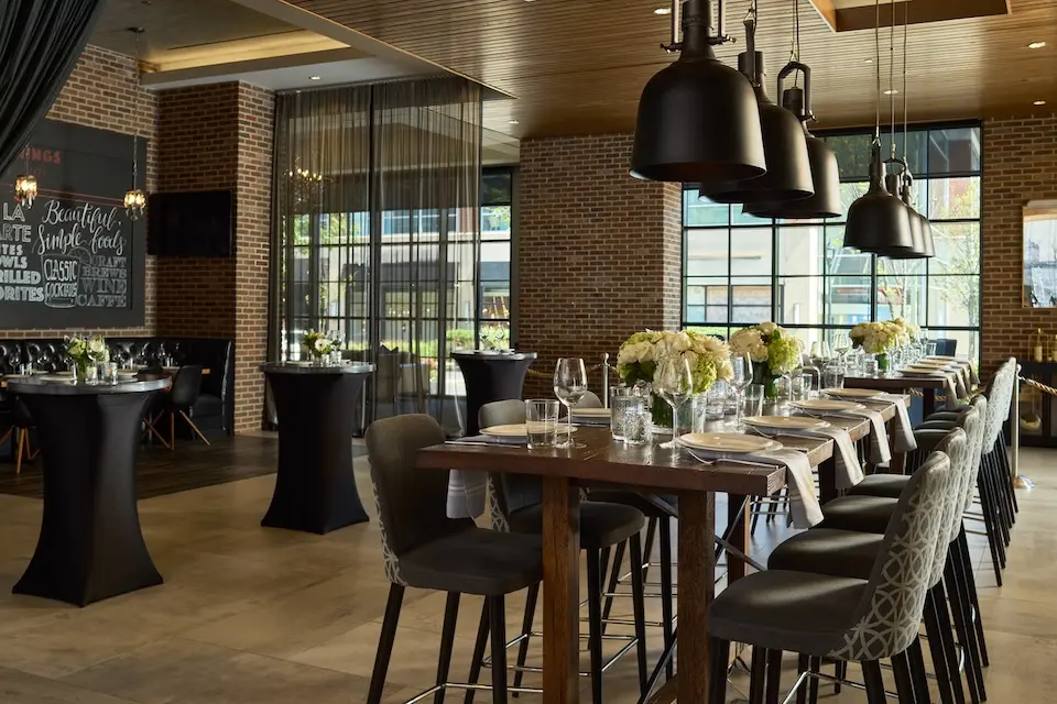 AKB - restaurant event space featuring a long wooden communal table with glassware and black cocktail tables