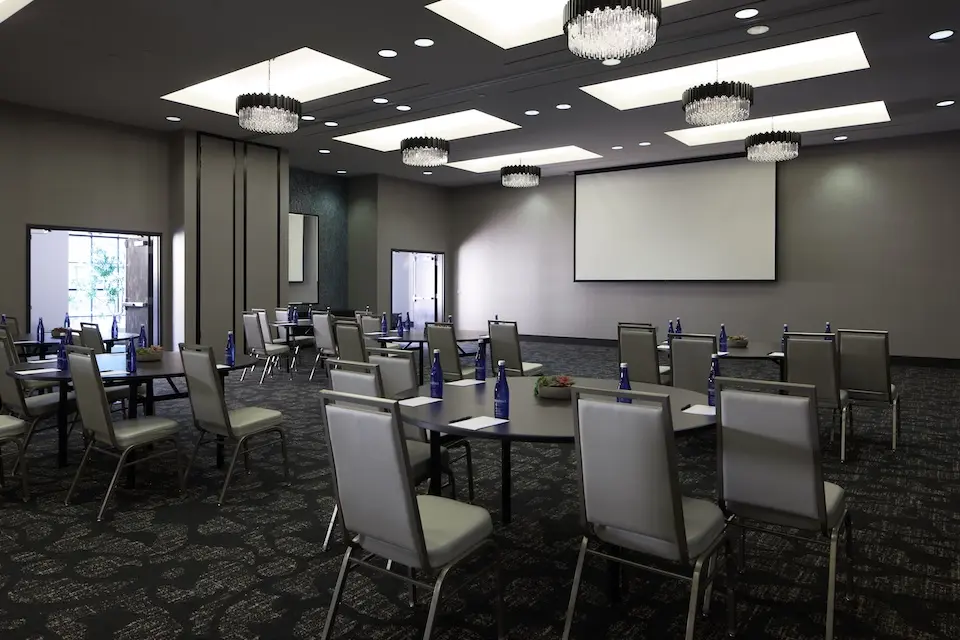 Great Room - corporate event with round tables and high-back chairs facing a projector screen