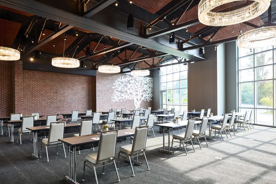 Great Room - classroom-style meeting setup featuring long rows of wooden tables, tan high-back chairs and floor-to-ceiling windows