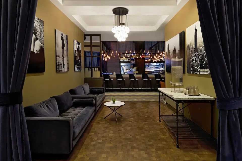 AKB - velvet sofas and a console table under a glass chandelier, leading into the adjacent AKB Hotel Bar