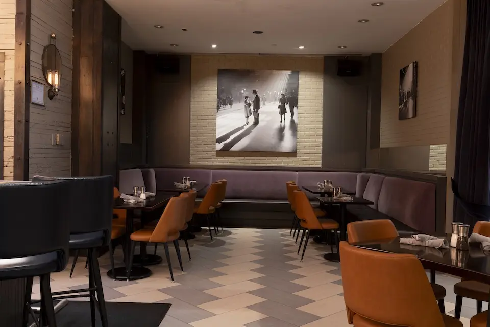 AKB - semiprivate dining alcove featuring banquette seating, orange upholstered chairs and New York-inspired wall art