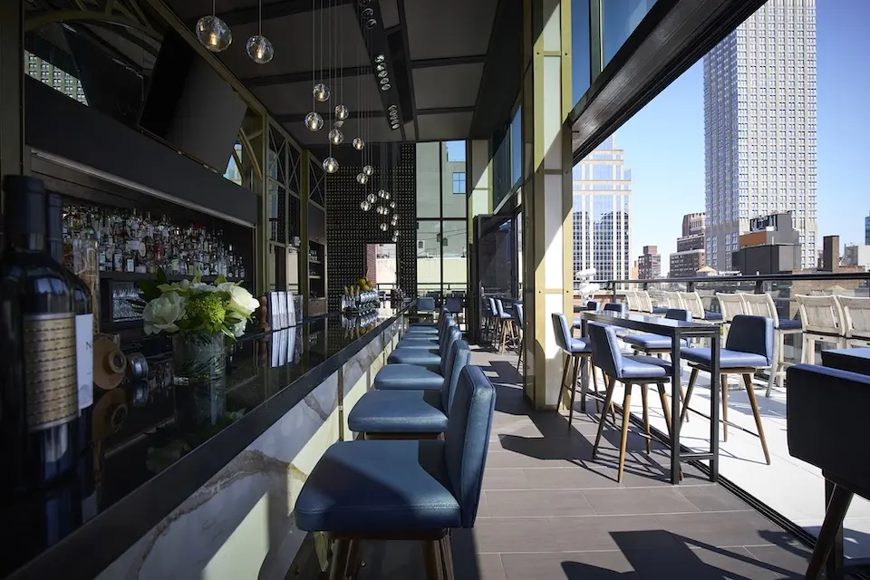 Spyglass - central bar with pendant lights, cobalt blue bar stools and an open-air terrace featuring Empire views