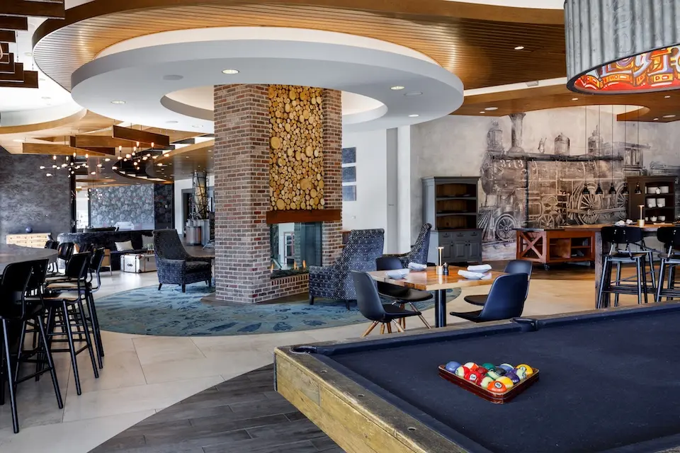 AKB - lounge area featuring a billiards table, table seating and a central brick fireplace under a circular recessed ceiling