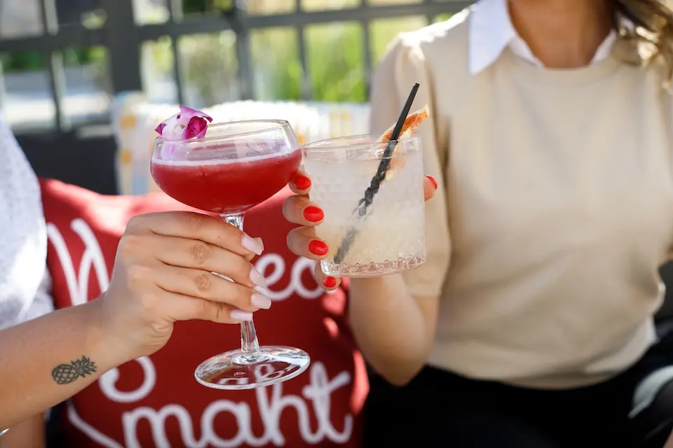 AKB - two women holding toasting cocktails on an outdoor patio