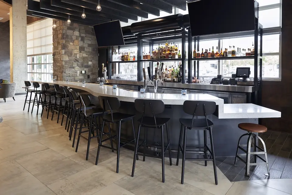 AKB - modern hotel bar featuring a long curved white countertop, black barstools and overhead TVs