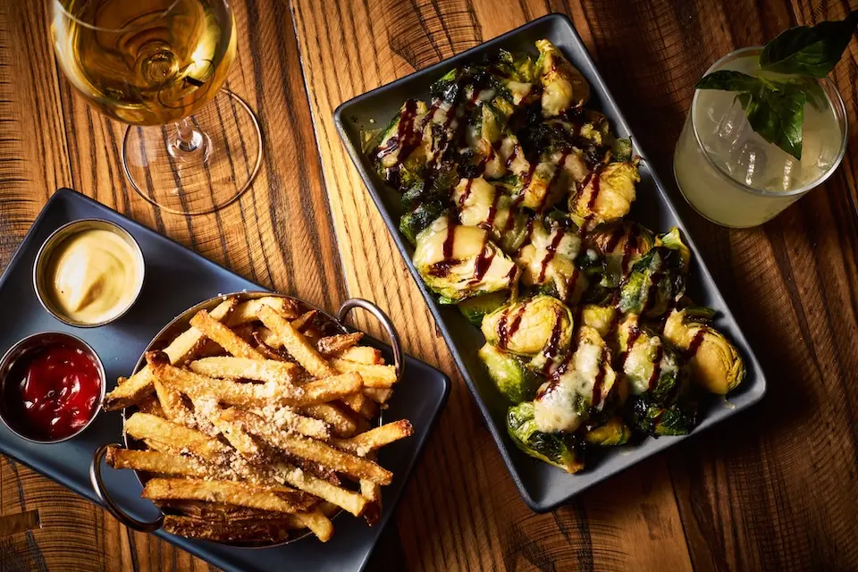AKB - shareable plates of hand-cut truffle fries and Brussels sprouts with a glass of white wine and a crafted cocktail