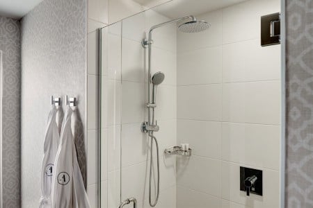 White porcelain tiled walk-in shower with two Frette robes hanging nearby