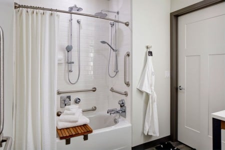 Mobility-accessible bathroom featuring a roll-in shower with shower seat, hand-held shower wand and grab bars