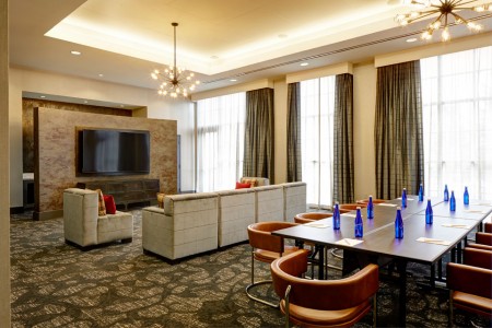 Hospitality Lounge — table with water bottles and chairs, plus soft seating and a flat-screen TV