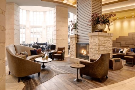 Lobby limestone fireplace with seating and Second Bar + Kitchen in the background
