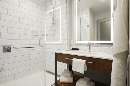 Modern bathroom with a subway-tiled walk-in shower and weathered iron vanity with lighted mirror