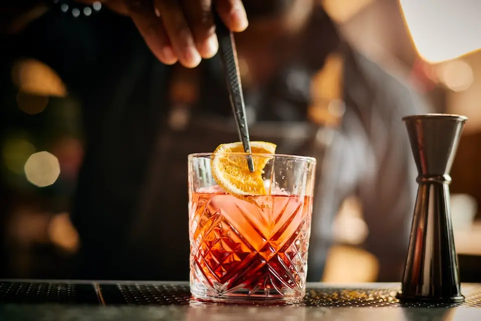 AKB - a bartender using tongs to place a fresh orange slice garnish on an old fashioned cocktail