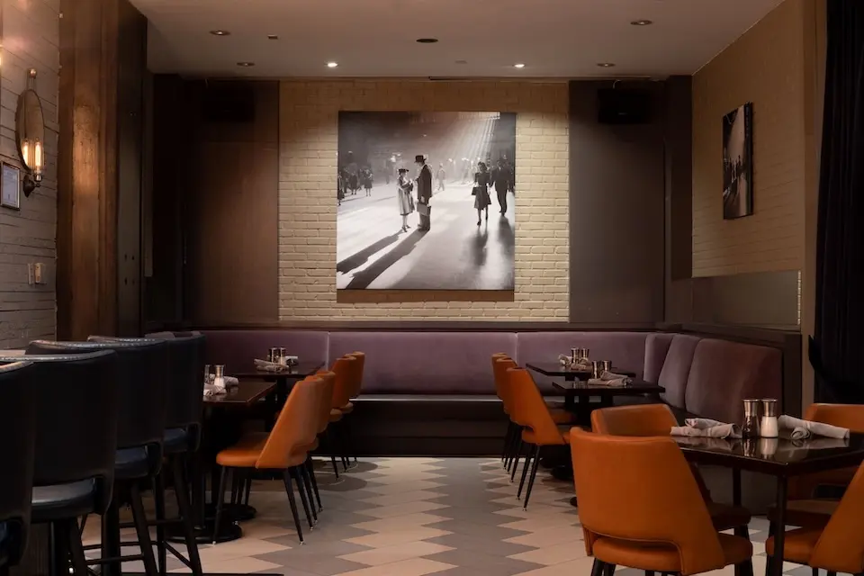 AKB - semiprivate dining alcove featuring banquette seating, orange upholstered chairs and a large New York-inspired black-and-white wall mural black-and-white wall mural