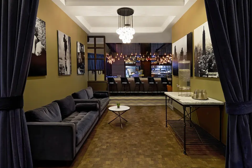 AKB - velvet sofas and a console table under a glass chandelier, leading into the adjacent AKB Hotel Bar