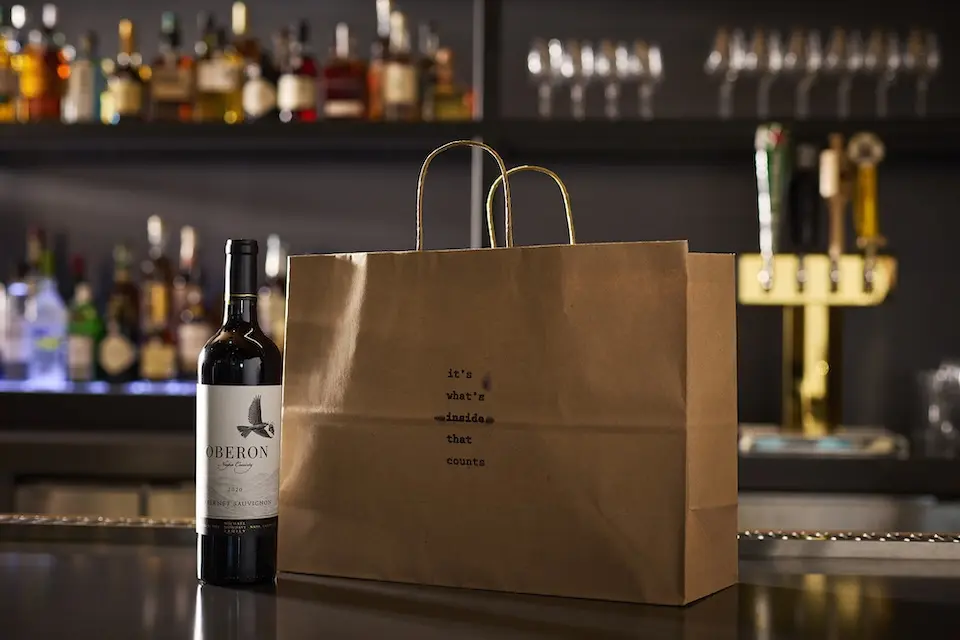 AKB - a brown paper takeout bag placed on a bar counter next to a bottle of wine