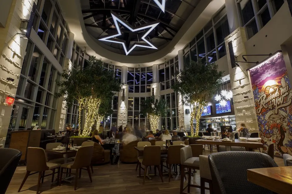 AKB - expansive indoor dining area featuring a central bar, lit trees, dining tables and a dramatic star-shaped light fixture mounted on an atrium ceiling