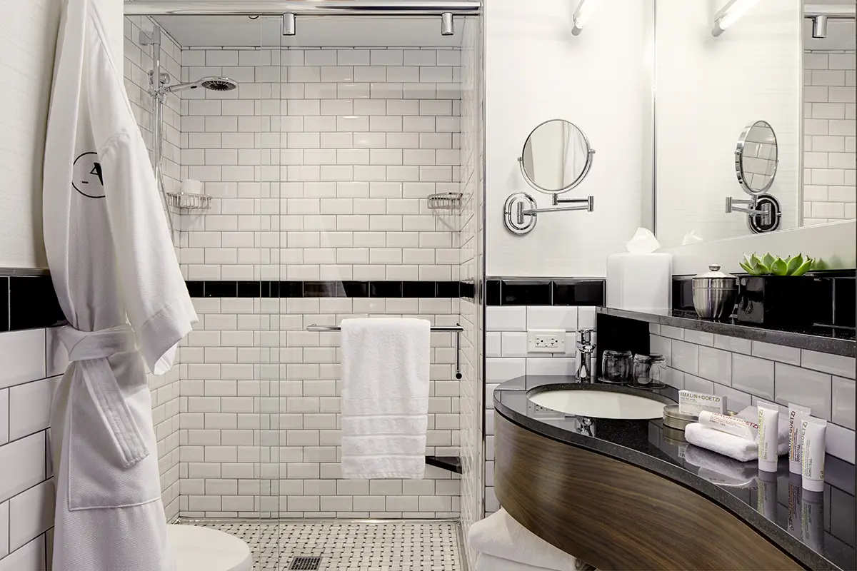 Elegant black-and-white subway-tile bathroom with sink, shower and Frette robe hanging