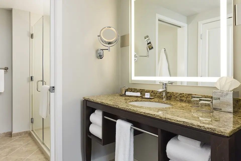 Archer's Den - modern bathroom featuring granite vanity with lighted mirror and tiled walk-in shower