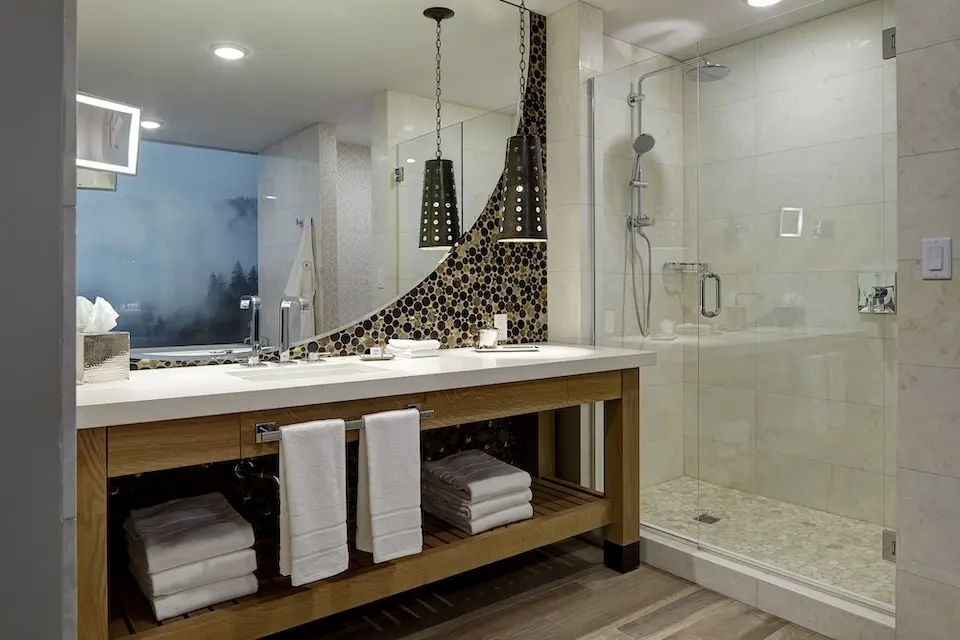 Archer King Balcony Suite - white marble vanity accented with a circular corner mirror with glass mosaic and a walk-in shower