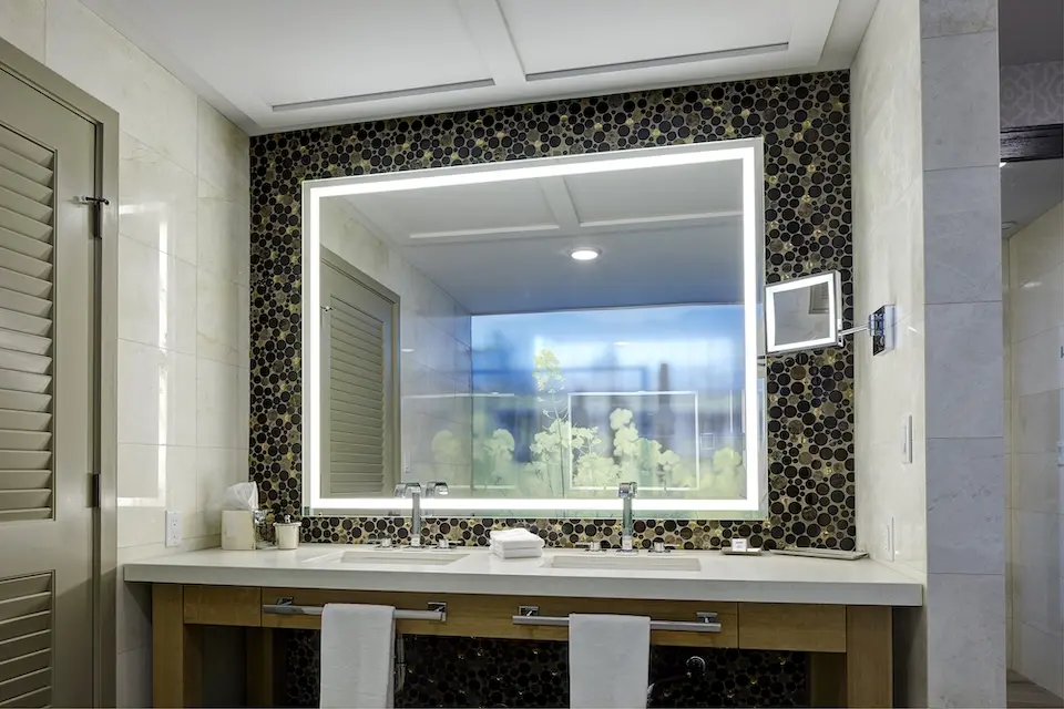 Archer's Den - white marble double vanity accented with a lit mirror against glass mosaic